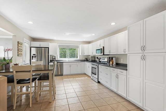 kitchen with dark countertops, white cabinetry, stainless steel appliances, recessed lighting, and light tile patterned flooring