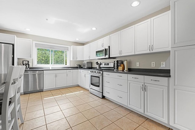 kitchen featuring white cabinets, dark countertops, appliances with stainless steel finishes, and light tile patterned floors