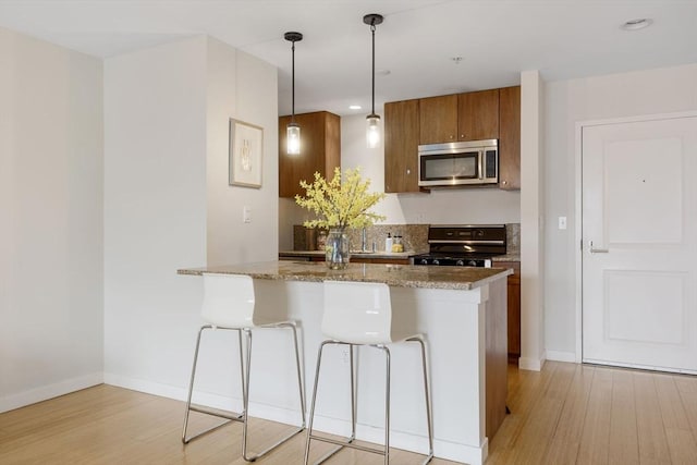 16 Miner St Unit 506, Boston, MA 02215 - kitchen featuring stainless steel microwave, stove, brown cabinetry, light wood-style flooring, and a breakfast bar