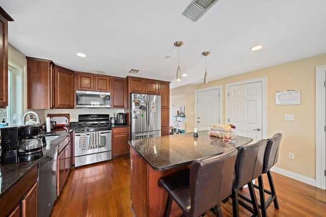 kitchen with appliances with stainless steel finishes, dark wood-style flooring, recessed lighting, a kitchen breakfast bar, and a center island