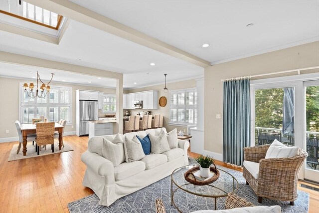 living room with crown molding, baseboards, a chandelier, visible vents, and light wood-style flooring