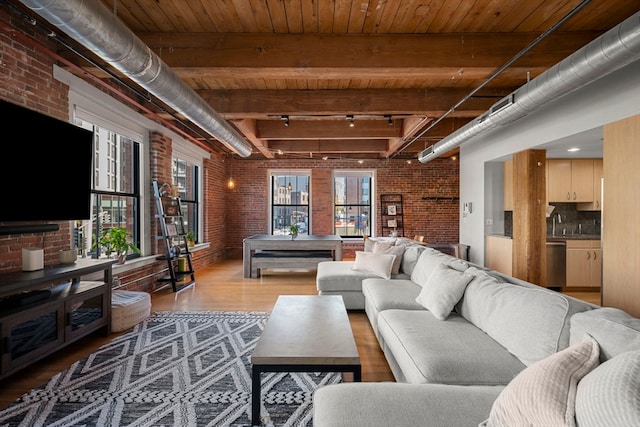 living room featuring light hardwood / wood-style flooring, beam ceiling, brick wall, and rail lighting