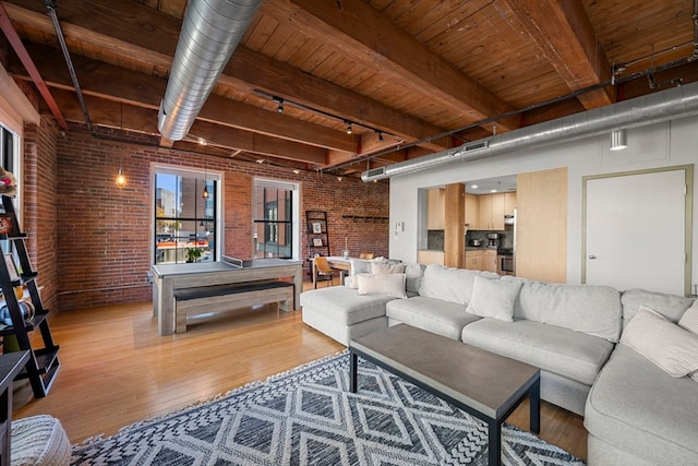 living room with beam ceiling, brick wall, track lighting, and light hardwood / wood-style flooring