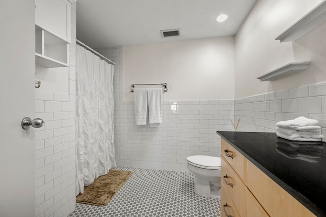 bathroom with toilet, vanity, tile patterned floors, and tile walls