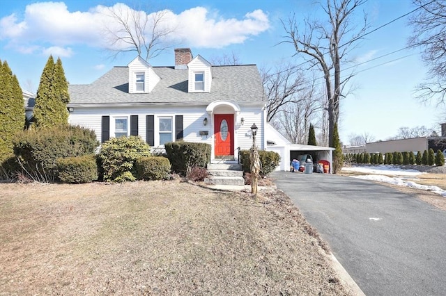 new england style home featuring aphalt driveway, an attached carport, a chimney, and a shingled roof