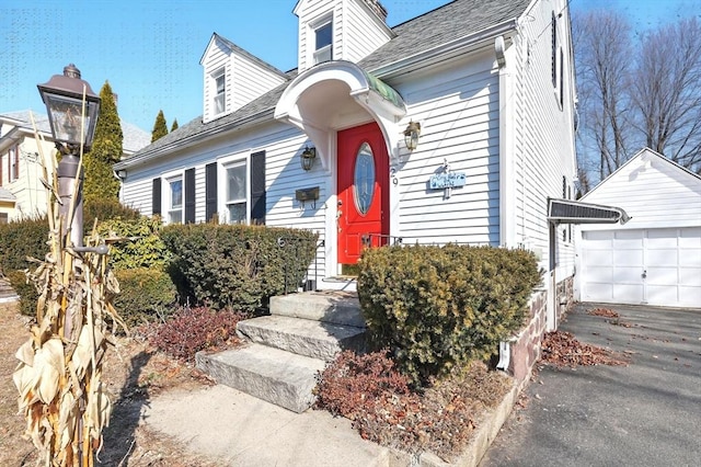 new england style home featuring an outbuilding, a garage, and a shingled roof