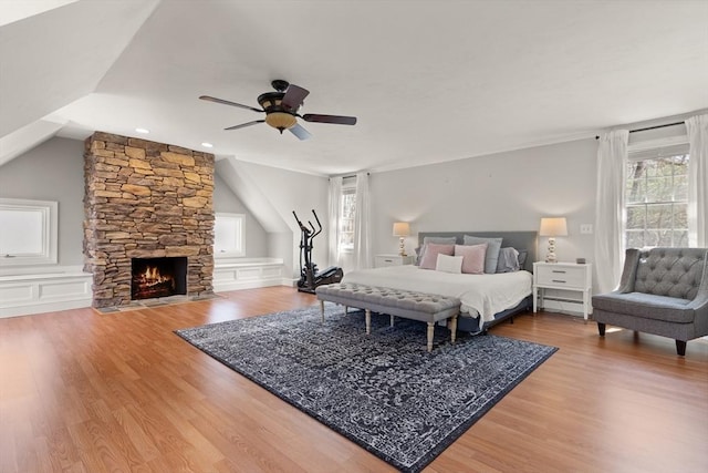 bedroom with lofted ceiling, wood finished floors, a fireplace, a baseboard heating unit, and a ceiling fan