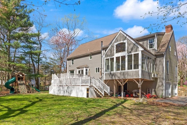 back of property with a wooden deck, a chimney, a sunroom, a lawn, and stairway