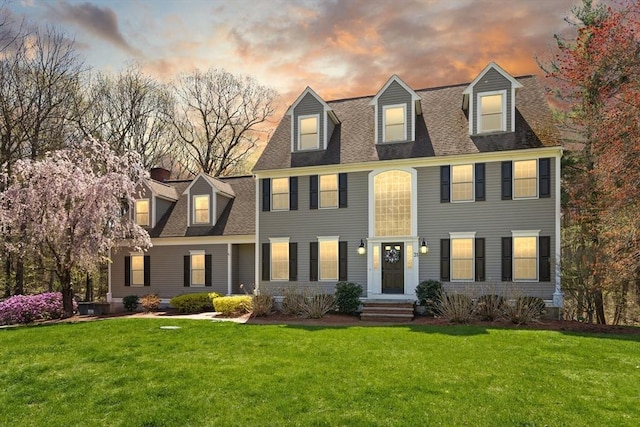 colonial inspired home featuring a shingled roof and a front lawn