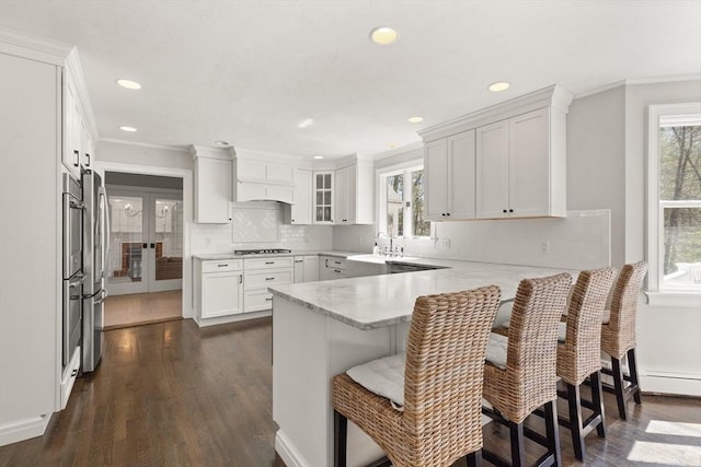 kitchen with crown molding, a sink, a peninsula, dark wood-style floors, and stainless steel appliances