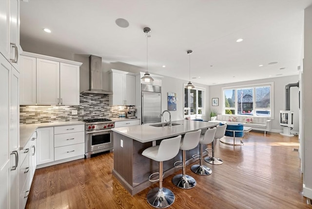 kitchen with high quality appliances, a sink, a kitchen breakfast bar, open floor plan, and wall chimney range hood