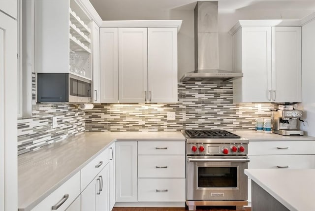 kitchen with wall chimney range hood, tasteful backsplash, white cabinetry, stainless steel appliances, and light countertops