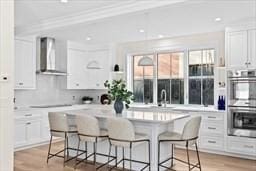 32 Kingsbury St Unit 1, Wellesley, MA 02481 - kitchen with ventilation hood, double oven, white cabinetry, a kitchen breakfast bar, and light countertops