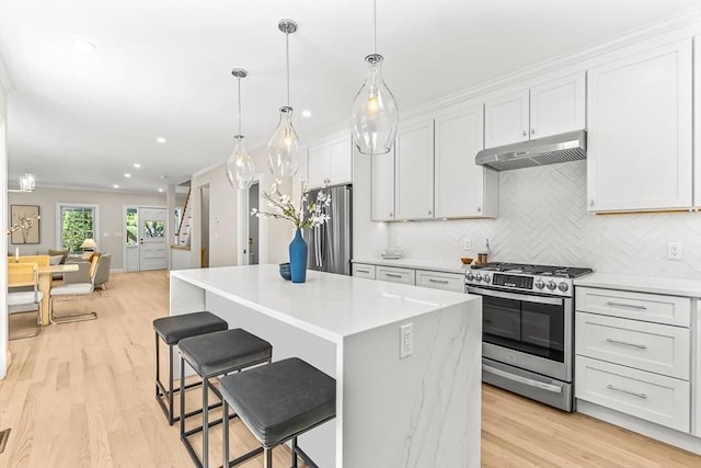 kitchen with under cabinet range hood, appliances with stainless steel finishes, decorative backsplash, and light wood-type flooring