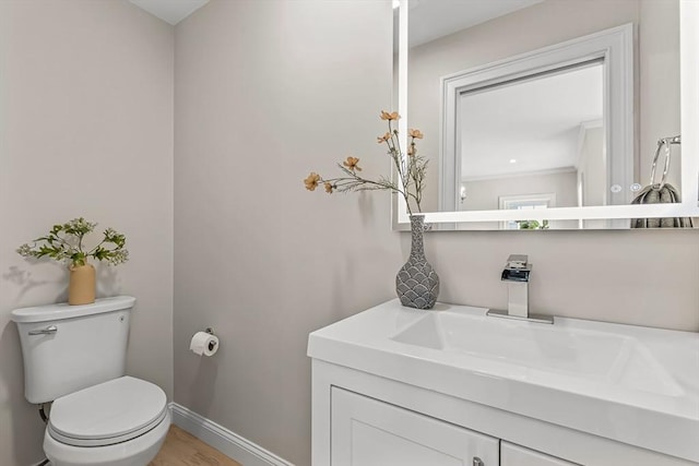 half bath with toilet, baseboards, wood finished floors, and vanity