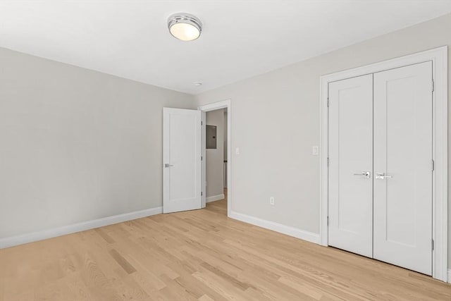 unfurnished bedroom with light wood-style floors, baseboards, electric panel, and a closet