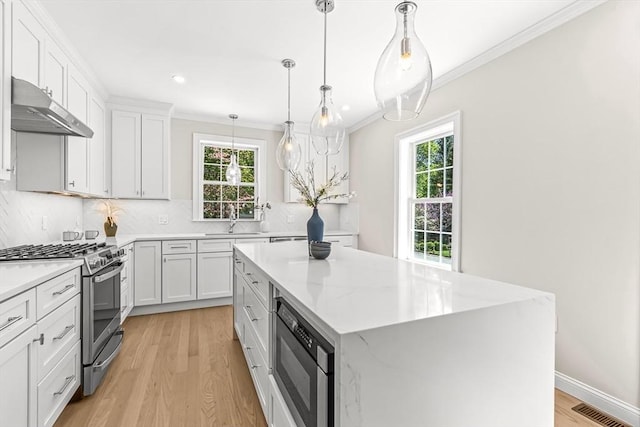 kitchen with a sink, stainless steel gas range oven, built in microwave, under cabinet range hood, and visible vents