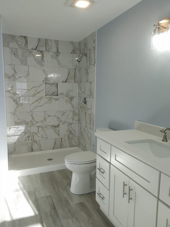 full bathroom featuring tiled shower, toilet, wood finished floors, and vanity