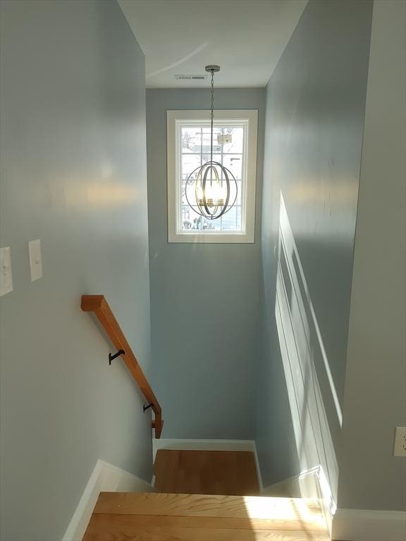 stairway with a notable chandelier, visible vents, baseboards, and wood finished floors