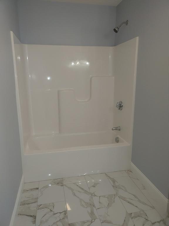 full bath with washtub / shower combination, marble finish floor, and baseboards