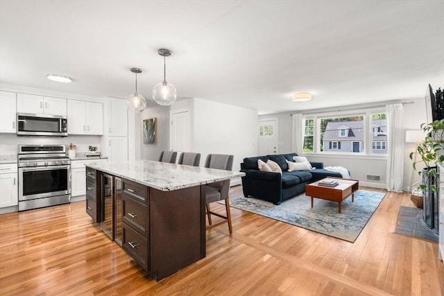 23 Redbird Rd, Wrentham, MA 02093 - kitchen featuring appliances with stainless steel finishes, a kitchen breakfast bar, white cabinets, beverage cooler, and light wood-style floors