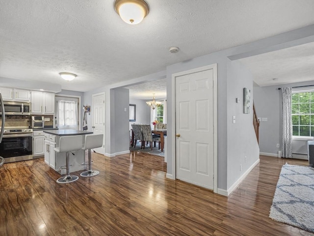 1056 Alger St, Winchendon, MA 01475 - kitchen with appliances with stainless steel finishes, a textured ceiling, a breakfast bar area, a kitchen island, and dark wood finished floors