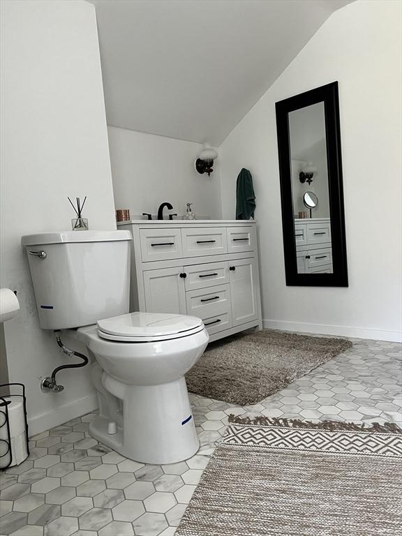 bathroom featuring vaulted ceiling, toilet, baseboards, and vanity