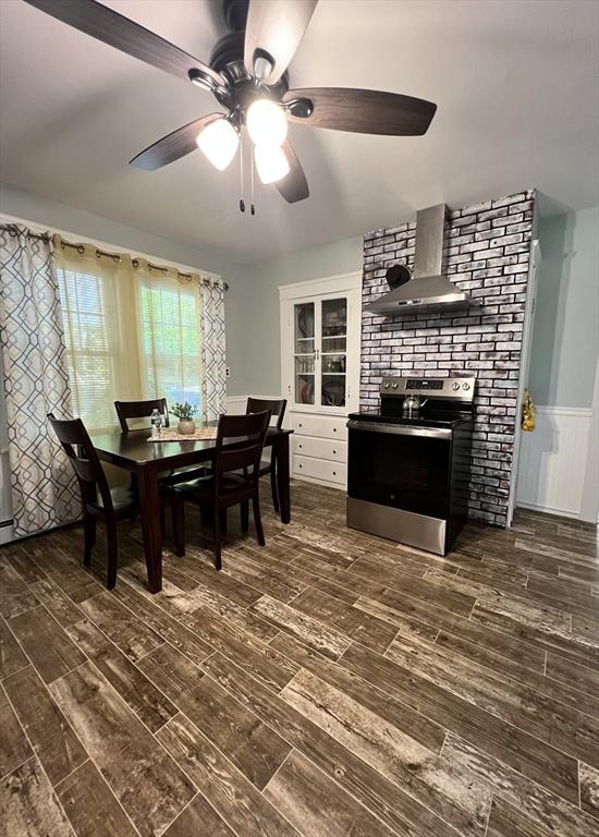 dining room featuring ceiling fan, a fireplace, dark wood finished floors, and a wainscoted wall