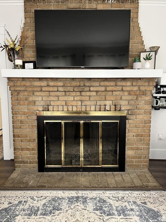 detailed view of a brick fireplace, wood finished floors, and baseboards