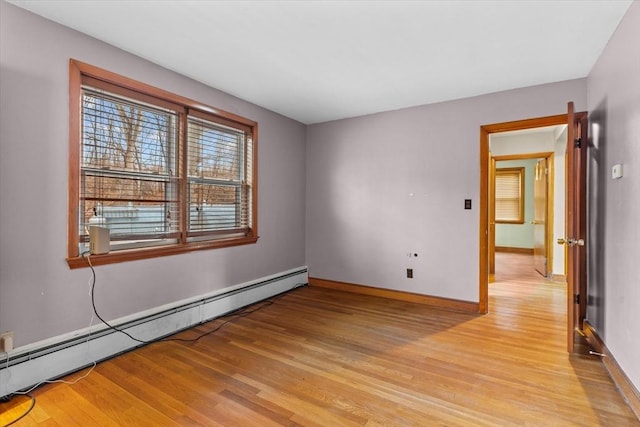 spare room with a baseboard heating unit, light wood finished floors, and baseboards