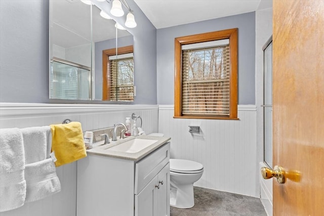 bathroom featuring toilet, a shower with door, vanity, and wainscoting