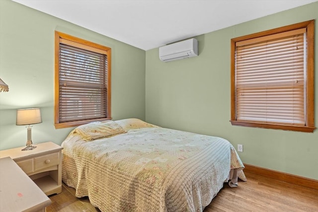 bedroom with an AC wall unit, multiple windows, and wood finished floors