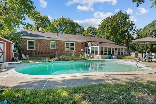 outdoor pool featuring a patio, a sunroom, an outbuilding, a storage unit, and a diving board