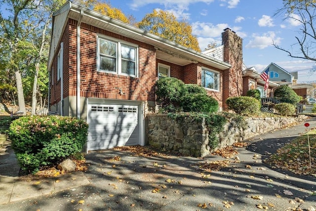 single story home featuring a garage, a chimney, aphalt driveway, and brick siding