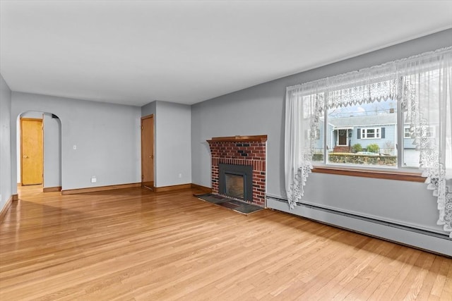 unfurnished living room with arched walkways, a fireplace, a baseboard radiator, light wood-style flooring, and baseboards