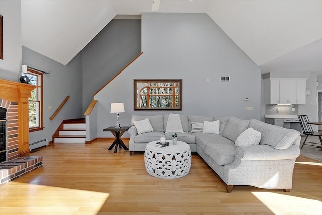 living area featuring visible vents, high vaulted ceiling, stairway, a baseboard radiator, and light wood finished floors