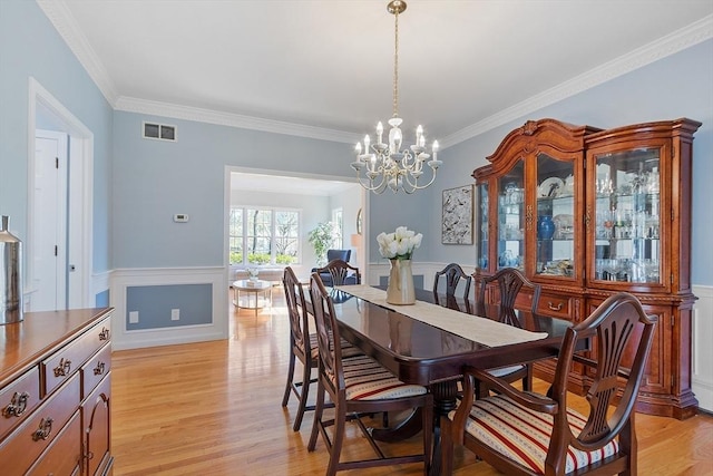 dining area with visible vents, light wood-style flooring, crown molding, and a notable chandelier