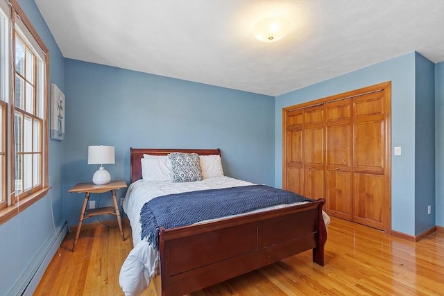 bedroom with a closet, light wood-style flooring, a baseboard heating unit, and multiple windows