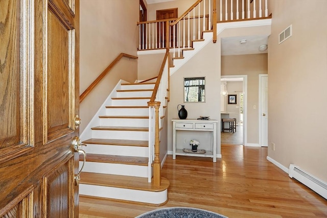 stairway with visible vents, a towering ceiling, wood finished floors, baseboards, and a baseboard heating unit