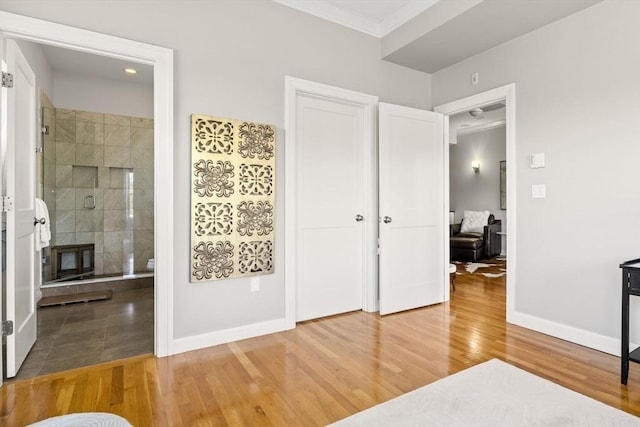 bedroom with crown molding, wood finished floors, baseboards, and ensuite bath