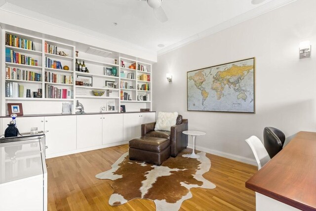 sitting room with light wood-style floors, a desk, crown molding, a ceiling fan, and baseboards