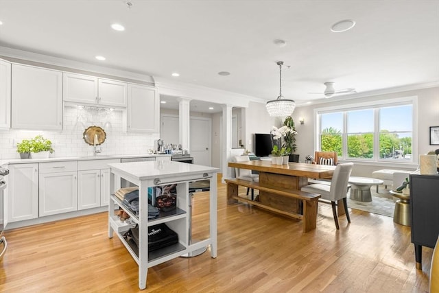 kitchen with light countertops, ornamental molding, ornate columns, white cabinets, and light wood finished floors