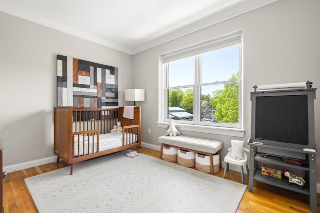 bedroom featuring ornamental molding, wood finished floors, baseboards, and a crib