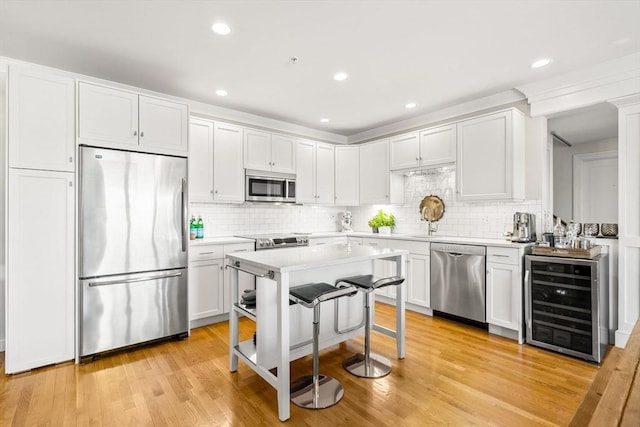 kitchen featuring stainless steel appliances, beverage cooler, light countertops, decorative backsplash, and white cabinets