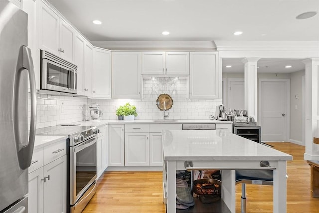 kitchen featuring stainless steel appliances, a sink, ornate columns, light wood-style floors, and backsplash