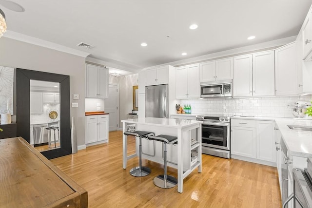 kitchen featuring appliances with stainless steel finishes, backsplash, light countertops, crown molding, and white cabinets