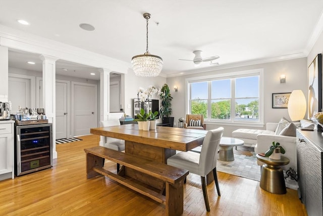 dining space with decorative columns, wine cooler, ornamental molding, light wood-style flooring, and a ceiling fan