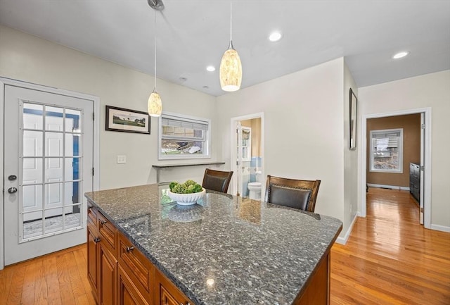 34 Prout St, Quincy, MA 02169 - kitchen featuring brown cabinetry, light wood-style flooring, a kitchen island, hanging light fixtures, and dark stone countertops