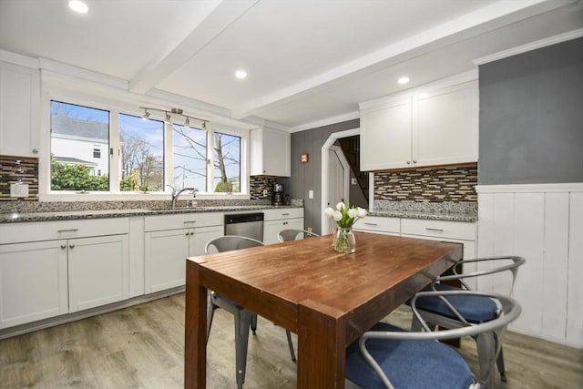 kitchen with light wood-style flooring, beamed ceiling, white cabinets, and stainless steel dishwasher
