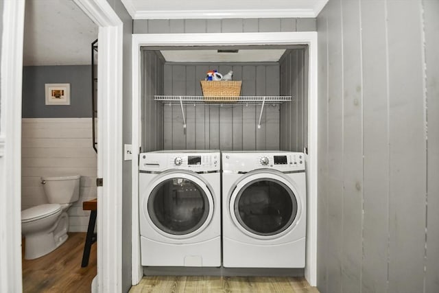 laundry area with laundry area, a wainscoted wall, wood finished floors, wooden walls, and washer and clothes dryer
